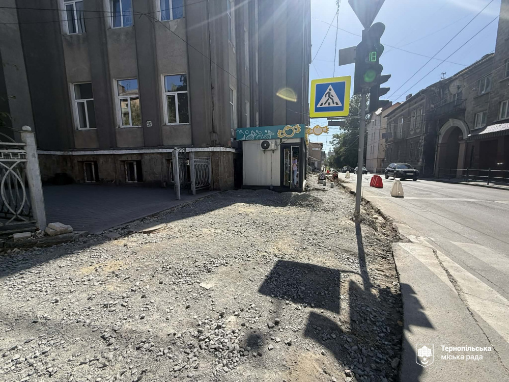 На кутовому перехресті біля чотириповерхової будівлі ділянку пішохідної зони засипано сірим щебенем і підготовлено до вкладання покриття.