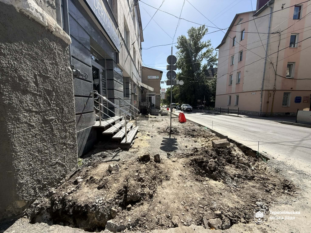 Біля будівлі з темно-сірим фасадом тротуар повністю розкопано до ґрунту та глини, через що рух пішоходів тимчасово ускладнено.